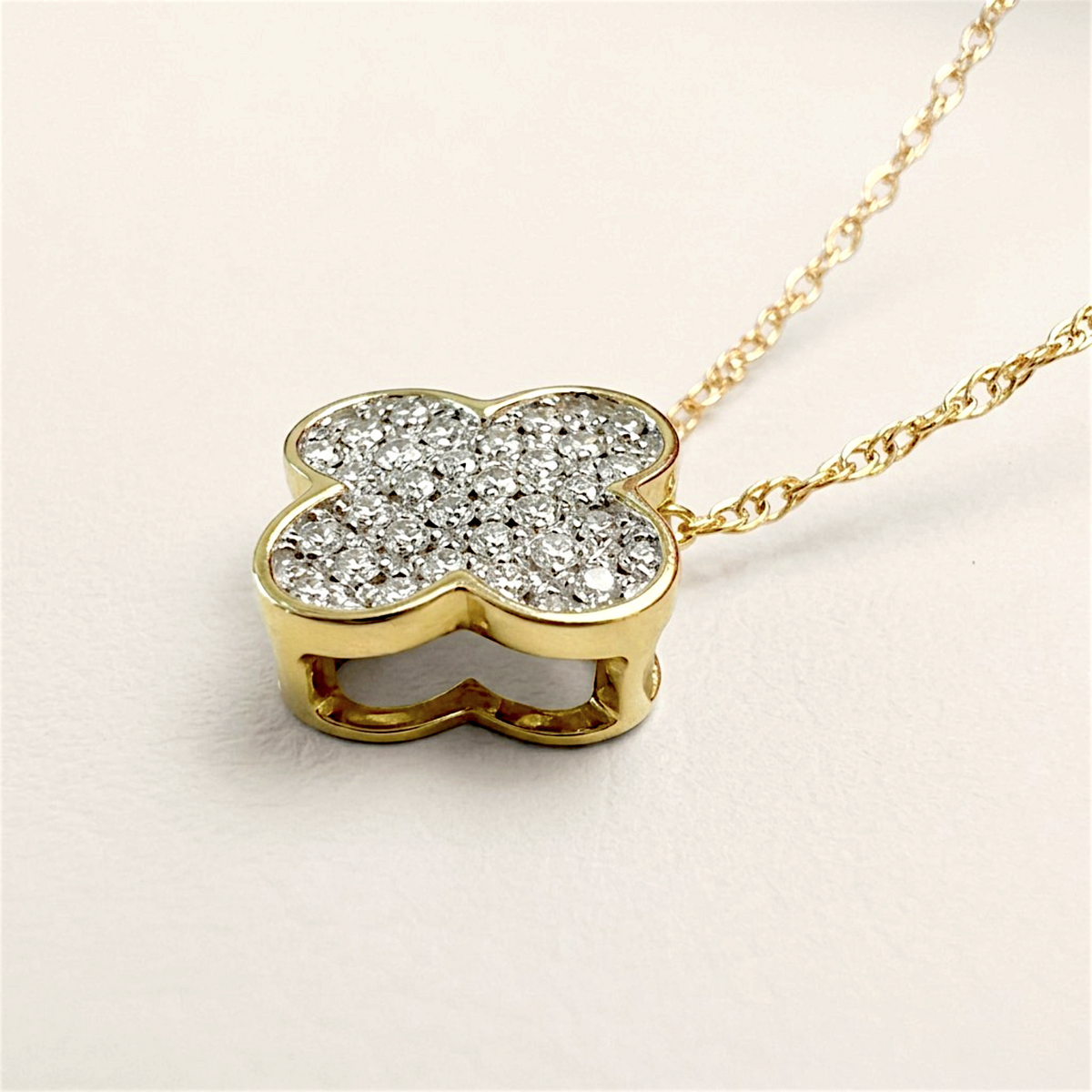 Angled close-up of the diamond clover pendant showing its polished gold border, open-sided setting, and chain links