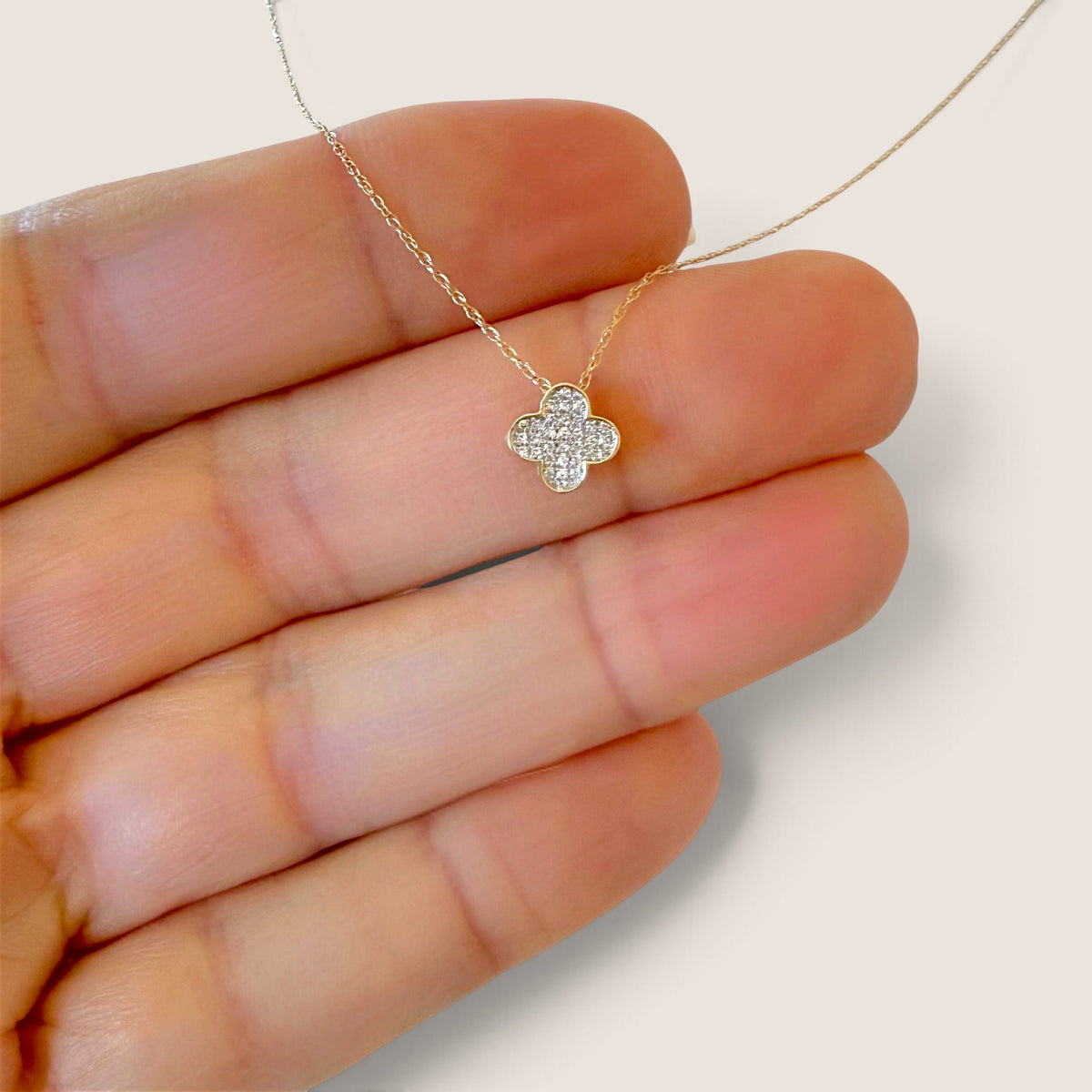 Petite diamond clover pendant resting against fingers to show its size, with the fine gold chain visible