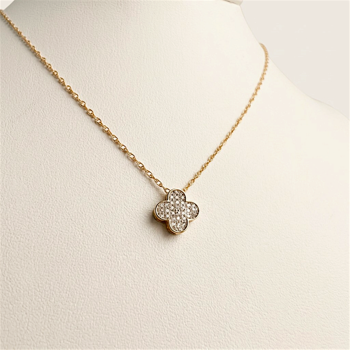 Diamond clover necklace draped on an ivory display bust, showing the pendant and gold chain