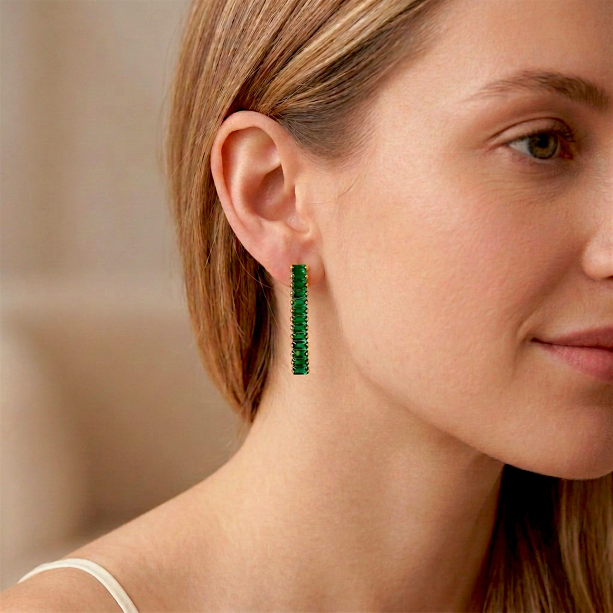 Close-up of a woman wearing an emerald-green baguette CZ drop earring with gold-tone settings.