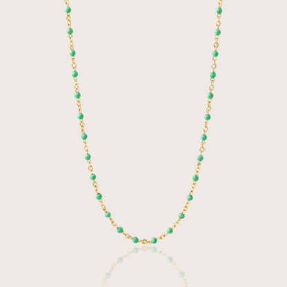 The 14K gold filled emerald green station necklace laid out flat on a premium neutral display, highlighting the high-polish mirror finish and vibrant enamel beaded chain links.