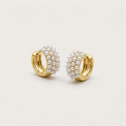 Pair of gold huggie earrings with clustered ivory freshwater pearls on a warm neutral background.
