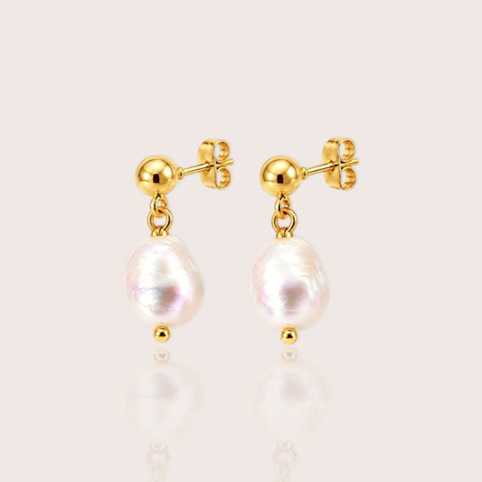 A pair of gold drop earrings featuring irregular white baroque pearls, displayed on a clean, light beige background with a soft reflection below.