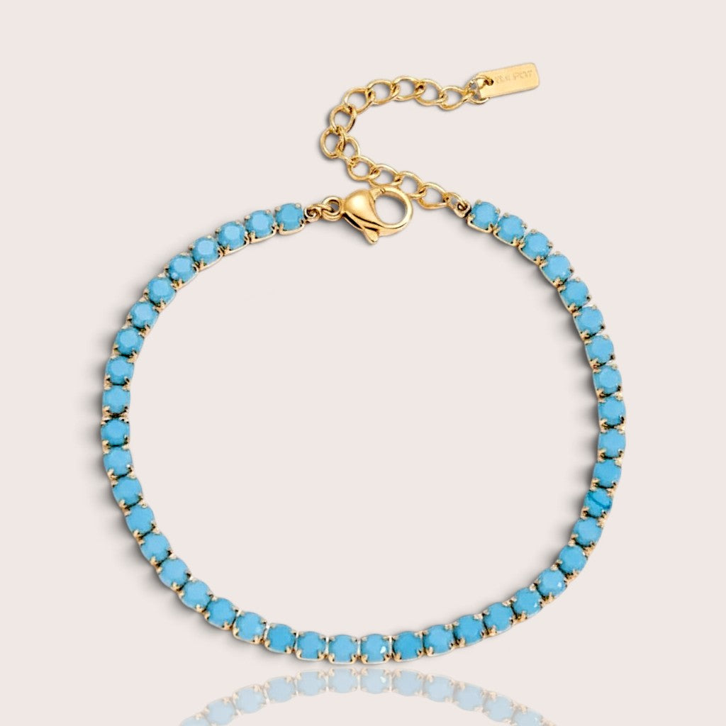 Dainty turquoise teal tennis bracelet in a tarnish-free gold prong setting on a clean backdrop.