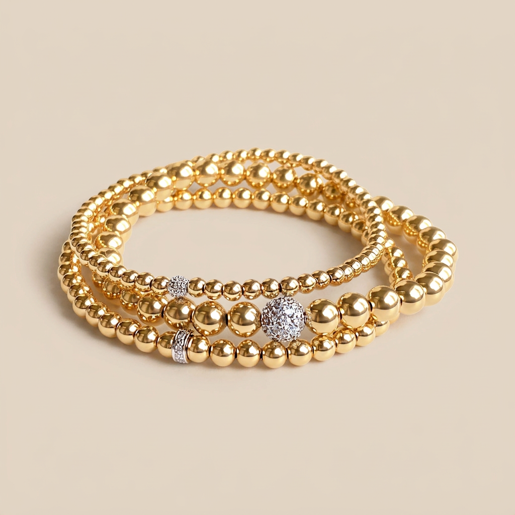 Three gold beaded bracelets with different bead sizes and diamond accents stacked on a light background