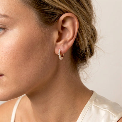 Woman wearing a small gold hoop with white pearls in her earlobe, with her hair swept back.