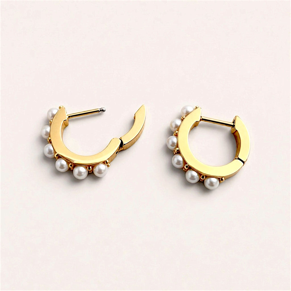 White pearl huggie hoops laid flat with hinged backs open, showing the posts and smooth inner gold surfaces.