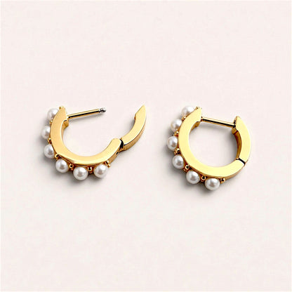 White pearl huggie hoops laid flat with hinged backs open, showing the posts and smooth inner gold surfaces.
