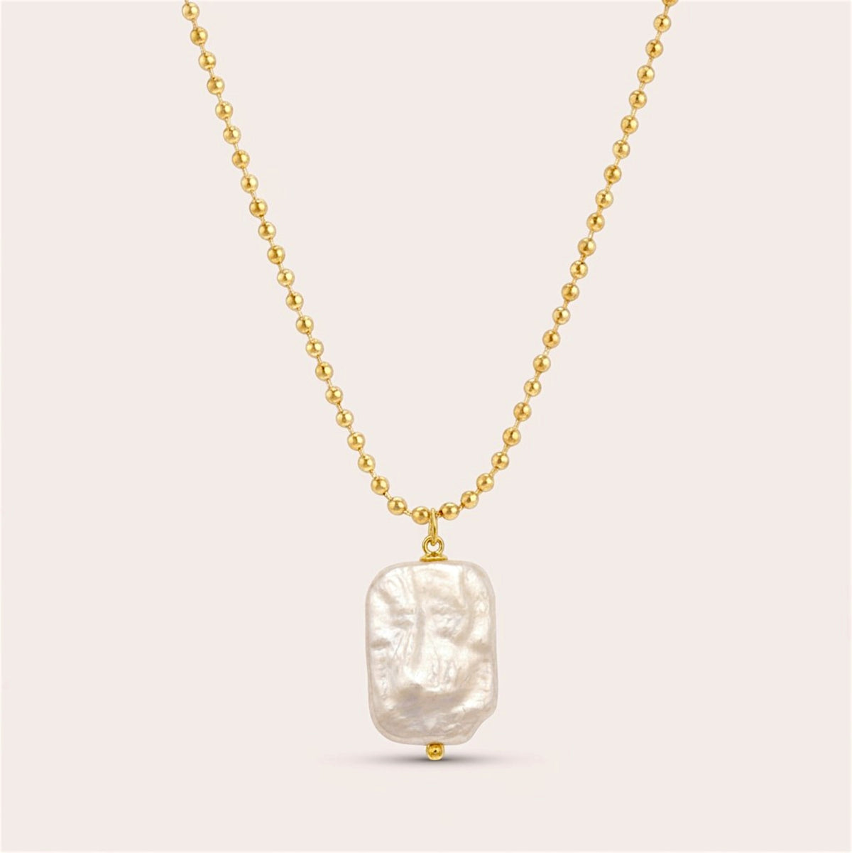 Gold ball chain necklace with an irregular rectangular freshwater pearl pendant on a warm neutral background.