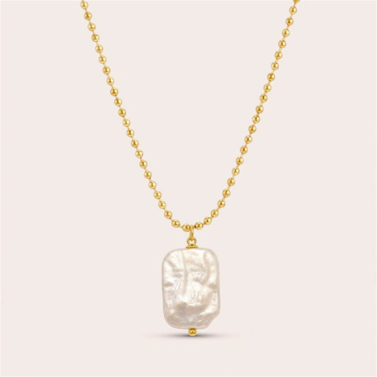 Gold ball chain necklace with an irregular rectangular freshwater pearl pendant on a warm neutral background.