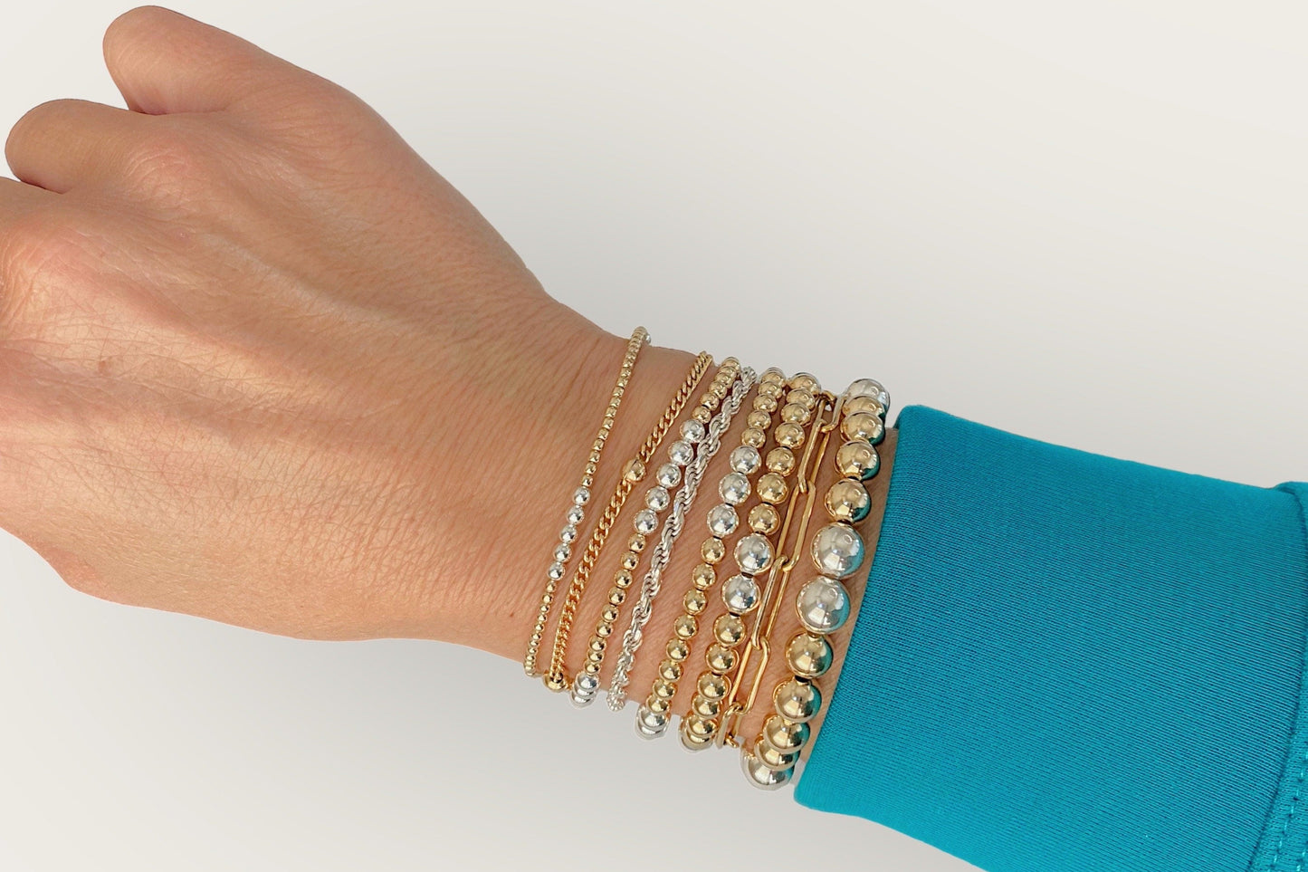 The Ashley Nicole Jewelry mixed metal two-tone bead bracelet styled on a model's wrist alongside separate all-gold and all-silver stacking bands.