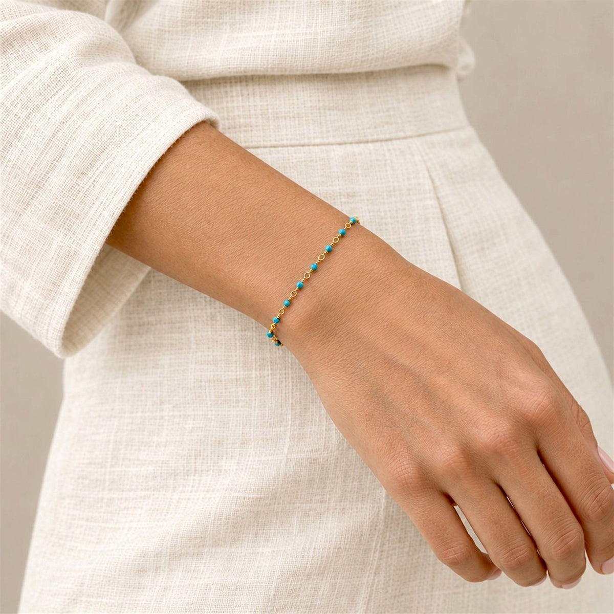 Delicate turquoise rosary chain bracelet worn alone on a wrist beside a denim 
