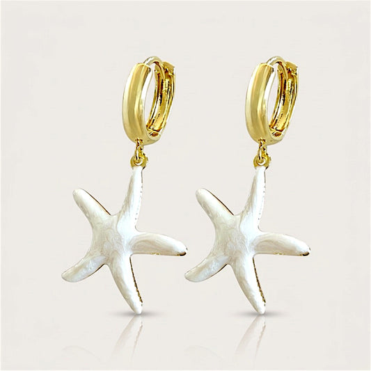 Pair of gold huggie hoop earrings with pearlescent white enamel starfish charms on a neutral background.