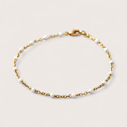 Gold chain bracelet with white beads on a light gray background