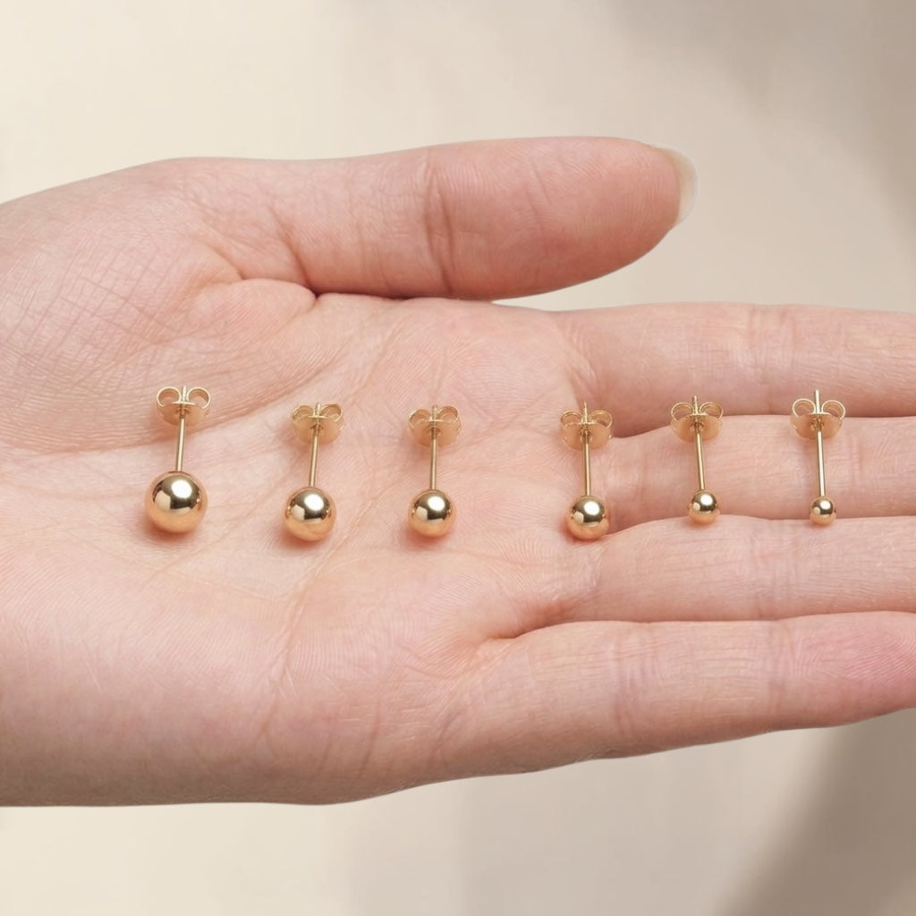 The hand scale size guide for the 14K gold-filled ball stud earrings showcased on a feminine hand. All six options—the new 2mm micro size, 3mm, 4mm, 5mm, 6mm, and 8mm sizes—are lined up perfectly on the fingers to provide a realistic, everyday comparison of their sizes.