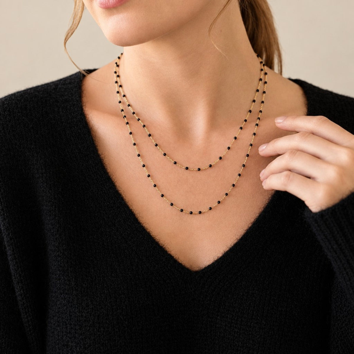 Model wearing two black enamel gold satellite necklaces layered at different lengths with a black V-neck top. 