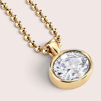 A gold ball-chain necklace with an oval bezel-set clear gemstone pendant, shown on a clean white background.