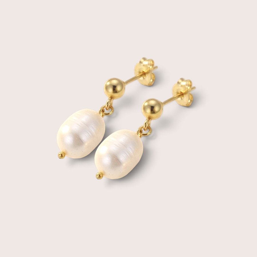 A pair of gold drop earrings featuring irregular white freshwater pearls, displayed on a light beige background.
