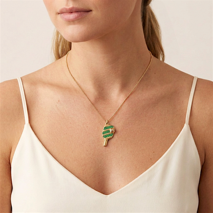 Woman in an ivory camisole wearing a gold necklace with a green cubic zirconia pickleball paddle-and-ball pendant necklace on a model.