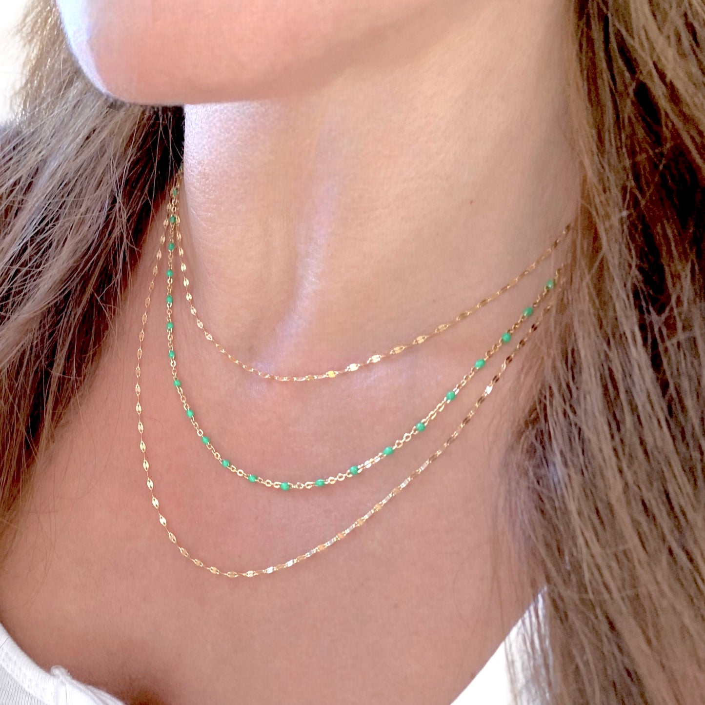 Close-up of a person wearing green and  gold necklace layered with other chains