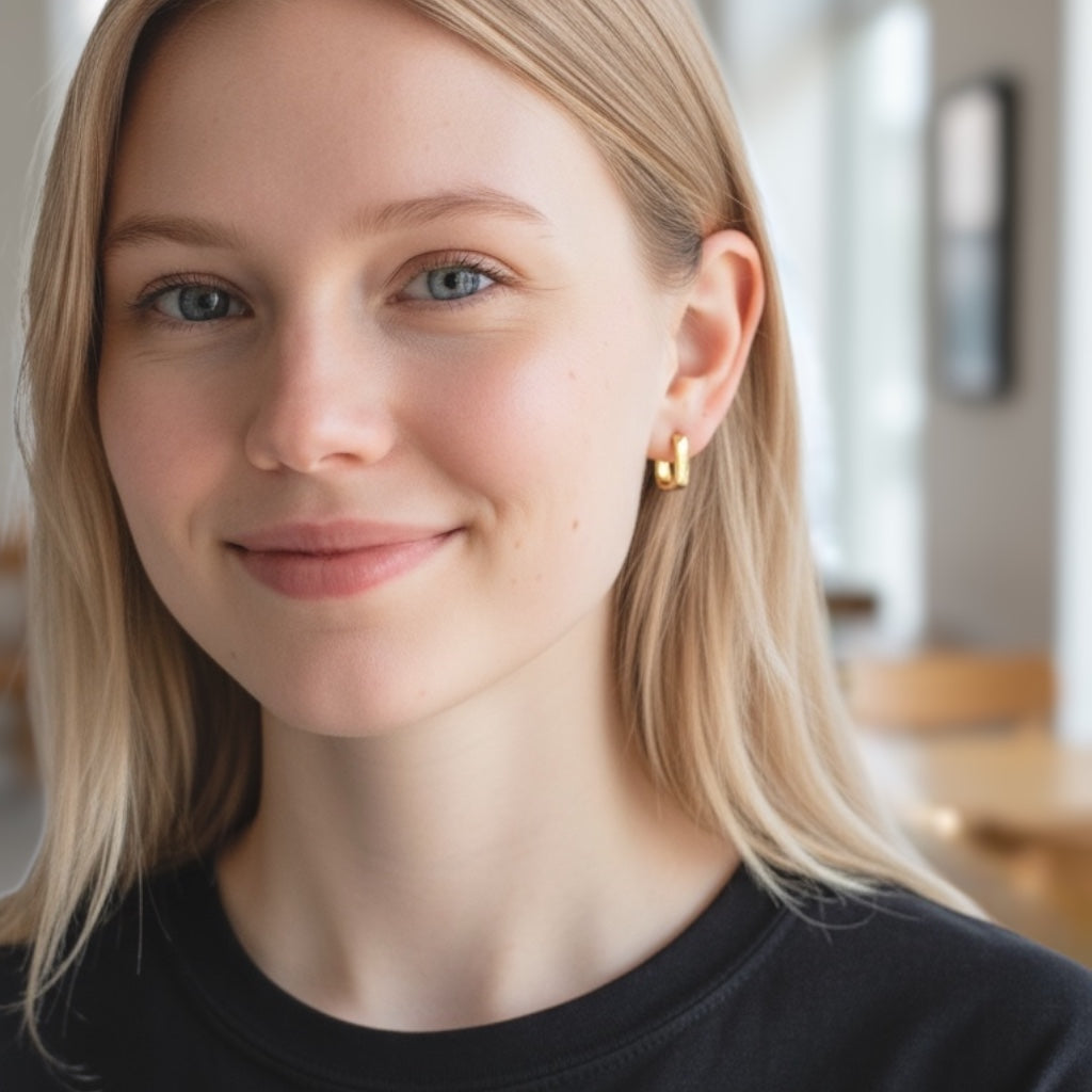 Model photo showing the 14mm x 12mm 18K gold plated rectangular huggie hoop earring being worn as a bold lobe piercing by a blonde woman.