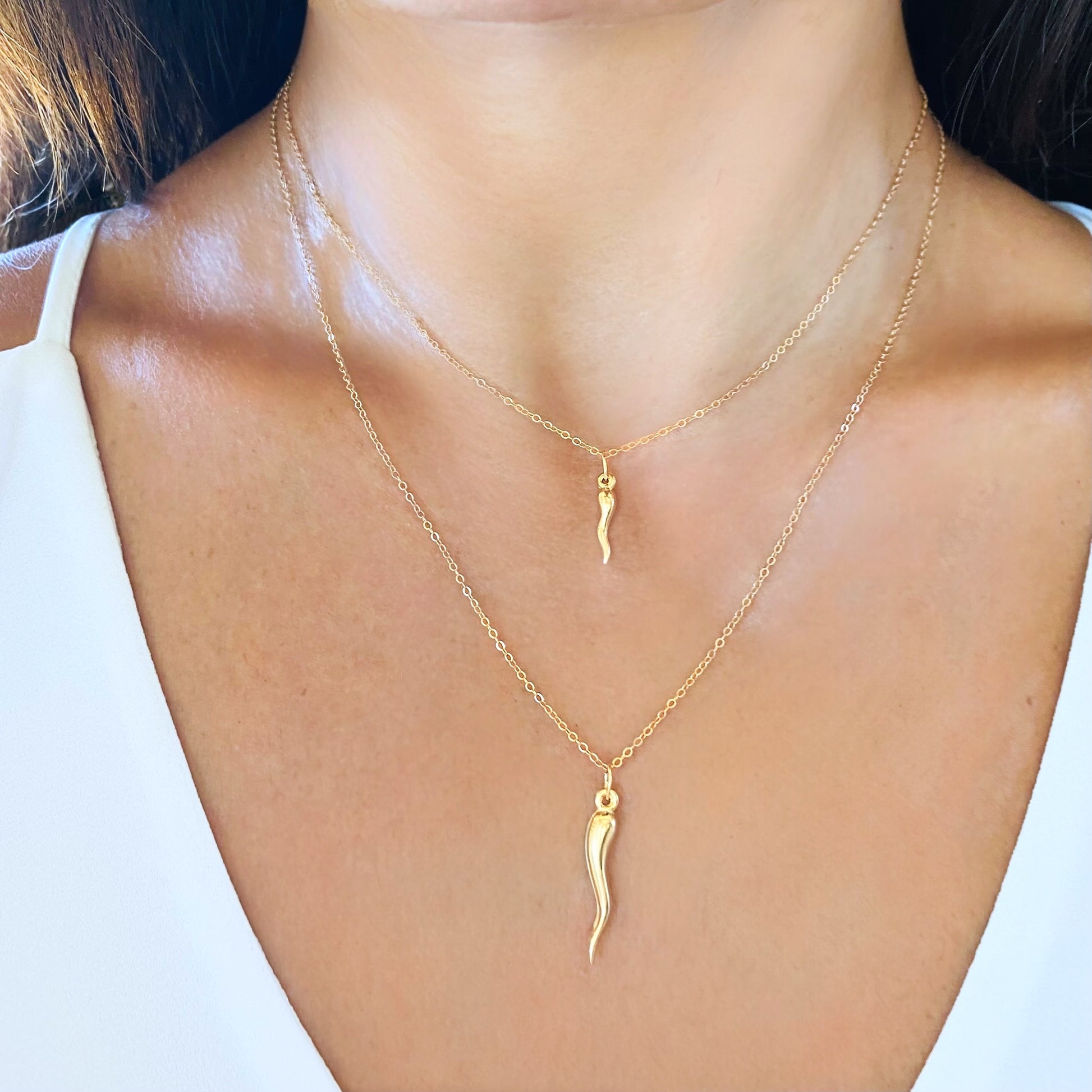 Woman layering small and large 14K gold Italian horn necklaces in 16 and 18 inch lengths