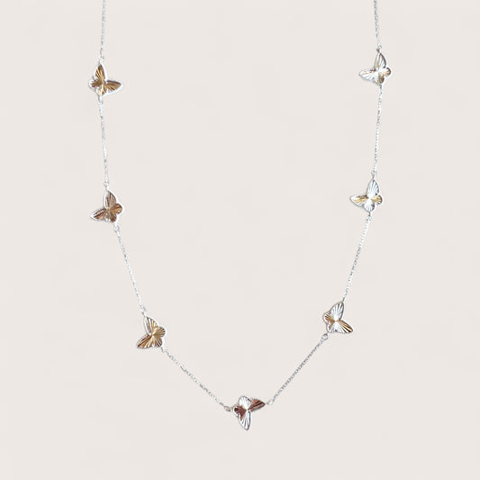 Flatlay image of a solid 925 sterling silver 7 motif butterfly charm station necklace with a sparkling diamond-cut faceted detail by Ashley Nicole Jewelry