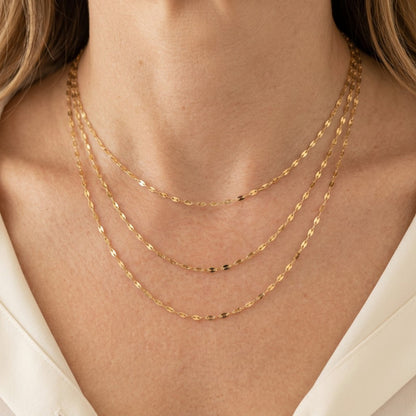 Three gold-filled mirror Valentino chain necklaces worn at different lengths above an ivory blouse