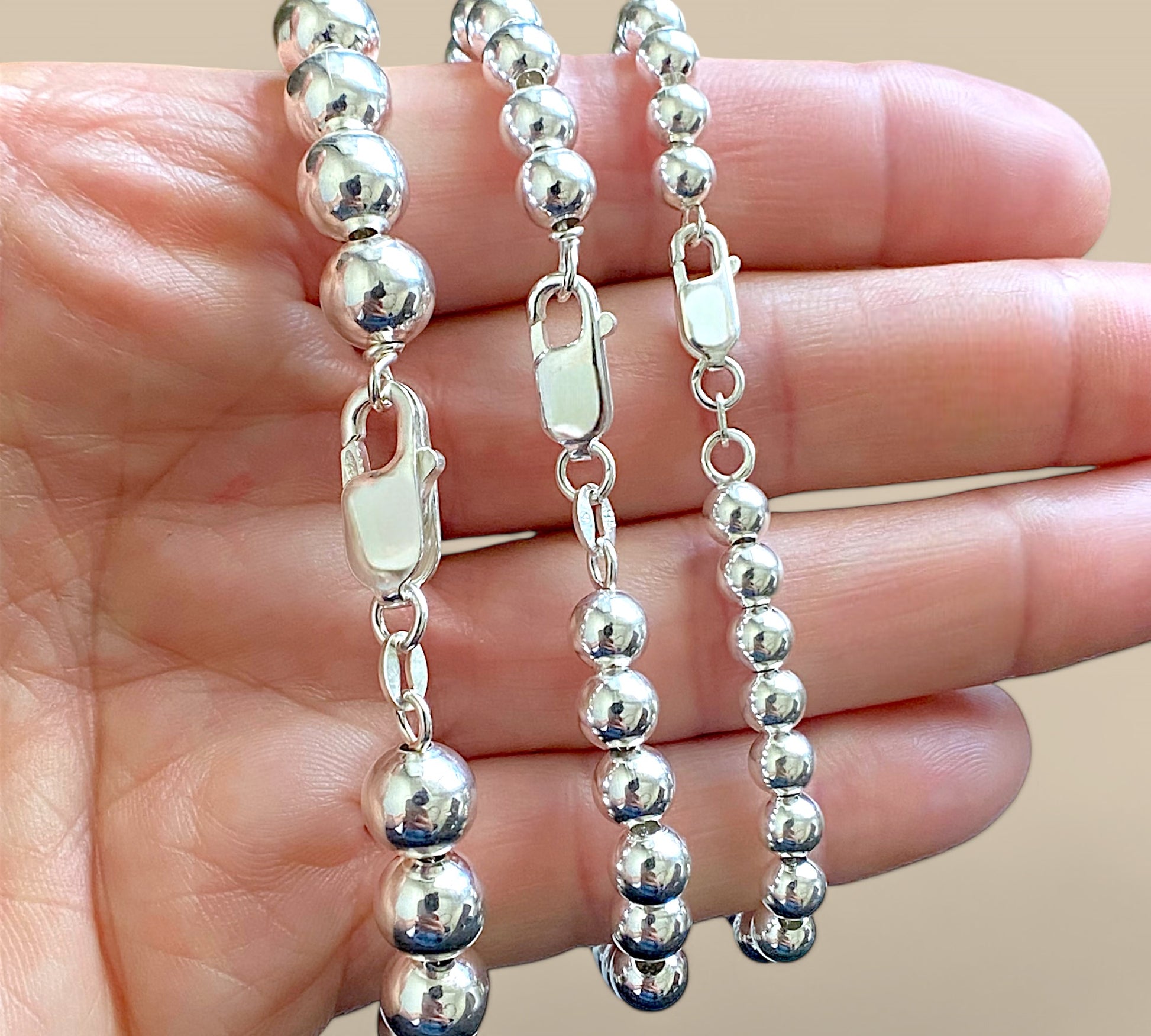 Close up of lobster clasps and  round silver beaded bracelets in a hand