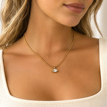 A close-up lifestyle shot of a woman wearing a delicate gold ball chain necklace with a small silver eye pendant, paired with a white scoop-neck t-shirt.