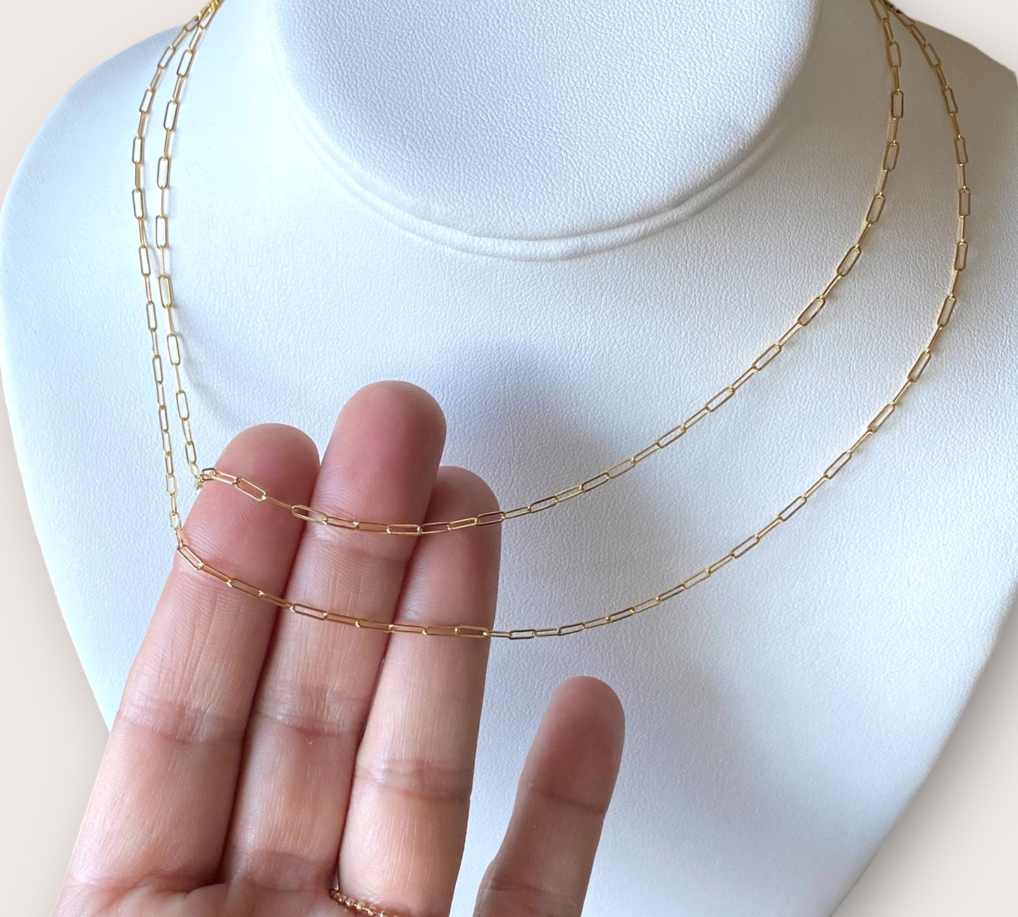 Close up of dainty 14K gold-filled flat link paperclip chain necklace styled in a layered everyday stack by Ashley Nicole Jewelry