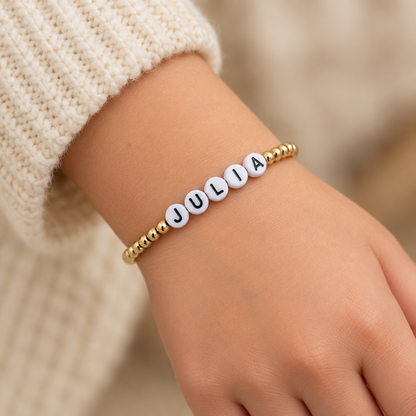 Close studio view of a custom name bracelet with gold-filled beads and white acrylic letter beads