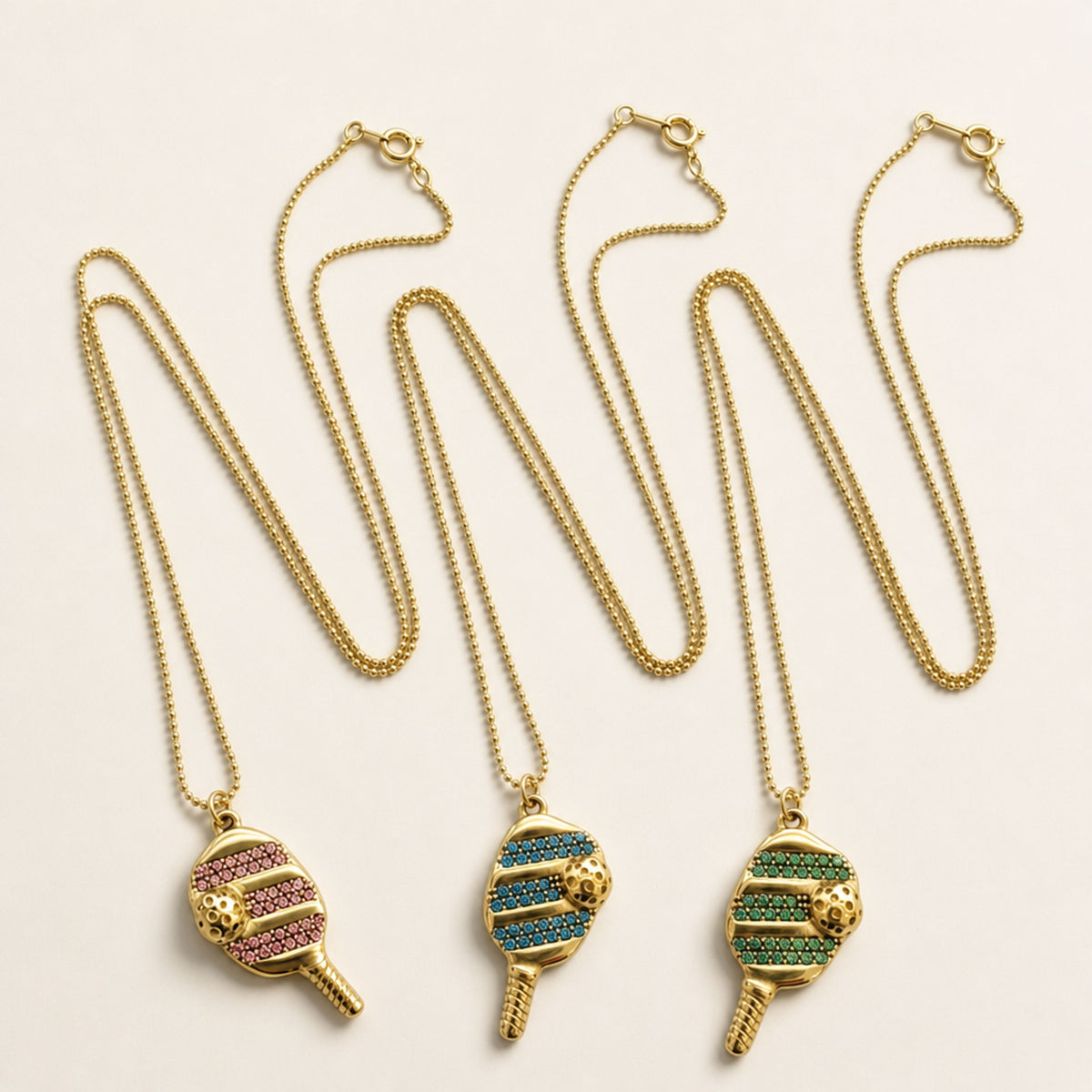 Pink, Blue, and Green pickleball necklace options displayed side by side, each with its own gold ball chain and spring-ring clasp.