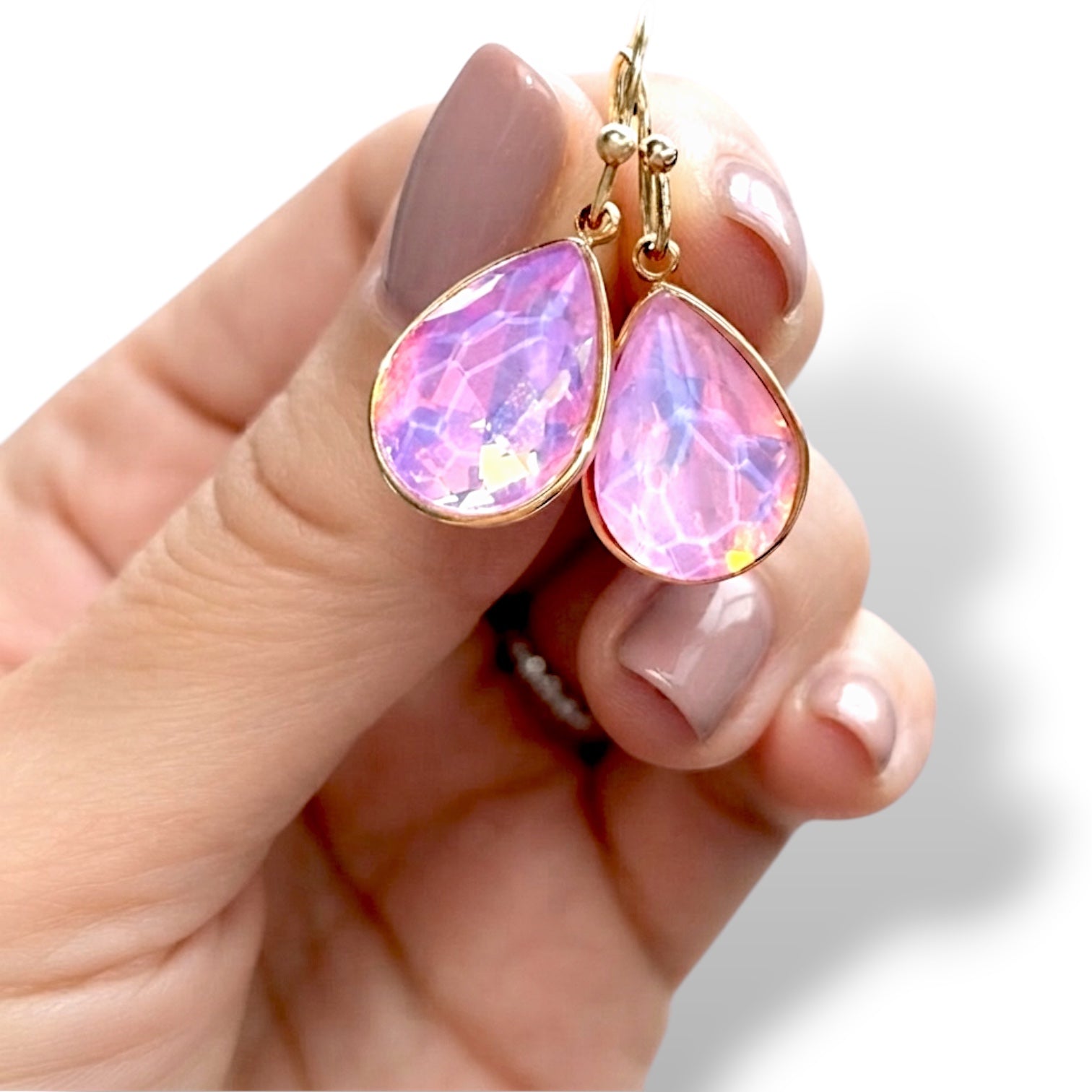 A close-up of  pair of pink opalescent crystal teardrop earrings with 14k gold-filled French wire hooks, 1-inch drop length in a persons hand.