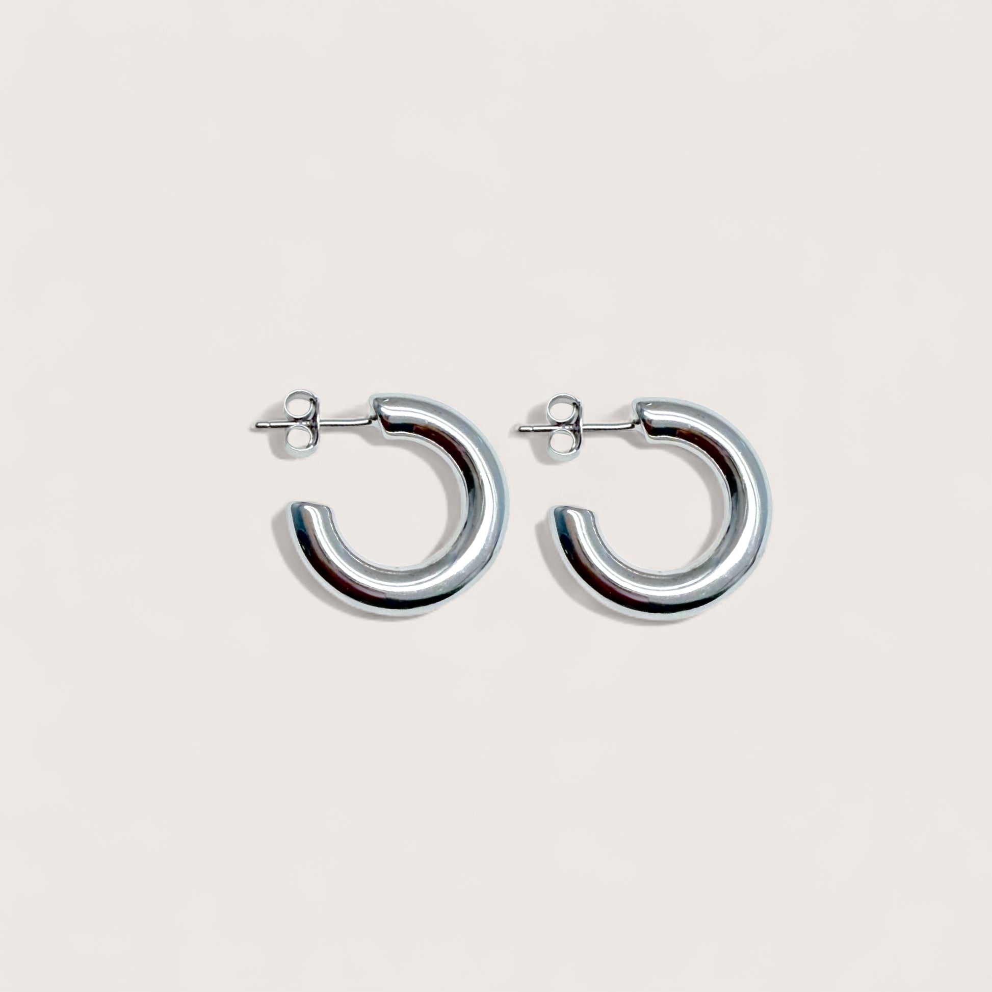 Studio lighting view of 4.2mm thick polished rhodium silver chunky hoops resting on a minimalist surface