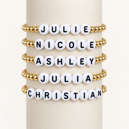 Five personalized kids’ name bracelets displayed with gold-filled beads and white letter beads