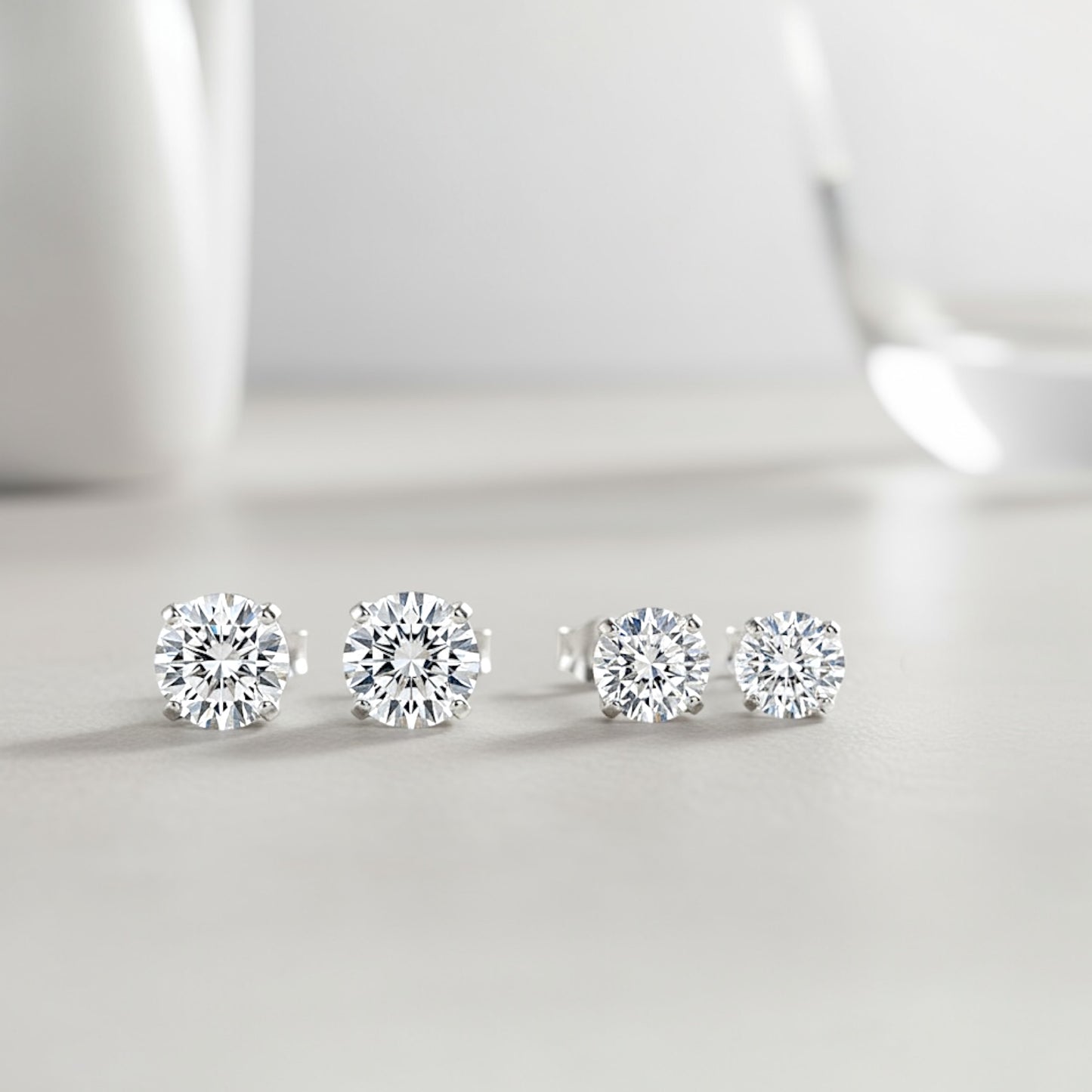 Rhodium Sterling Silver Moissanite Earrings on ear showing sizes side by side in 5mm (1.00CTW) – 0.50ct (DEW) . 6mm (1.60CTW) – 0.80ct (DEW) 