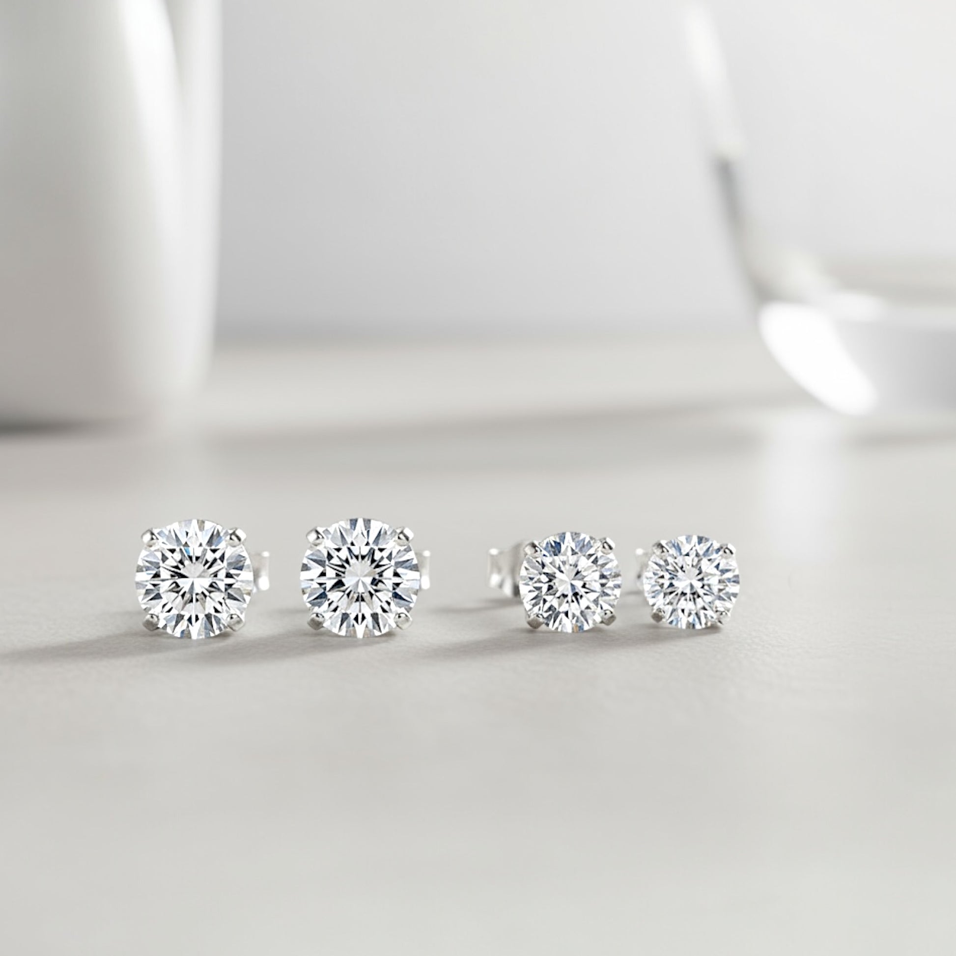 Rhodium Sterling Silver Moissanite Earrings on ear showing sizes side by side in 5mm (1.00CTW) – 0.50ct (DEW) . 6mm (1.60CTW) – 0.80ct (DEW) 