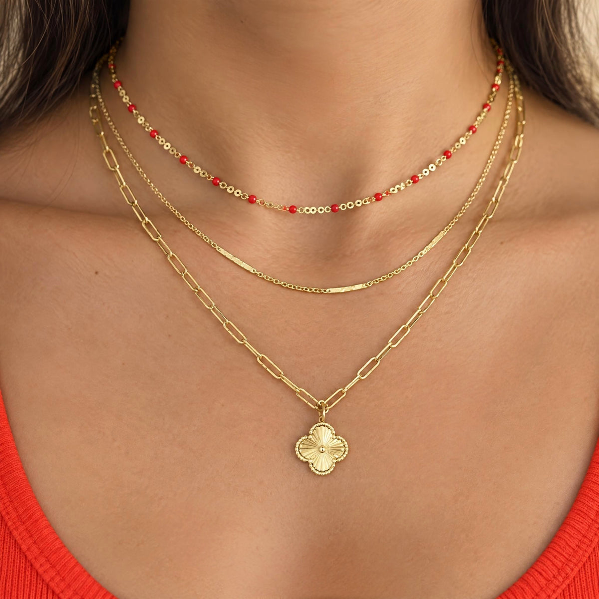 Red enamel station necklace layered with gold necklaces on a model