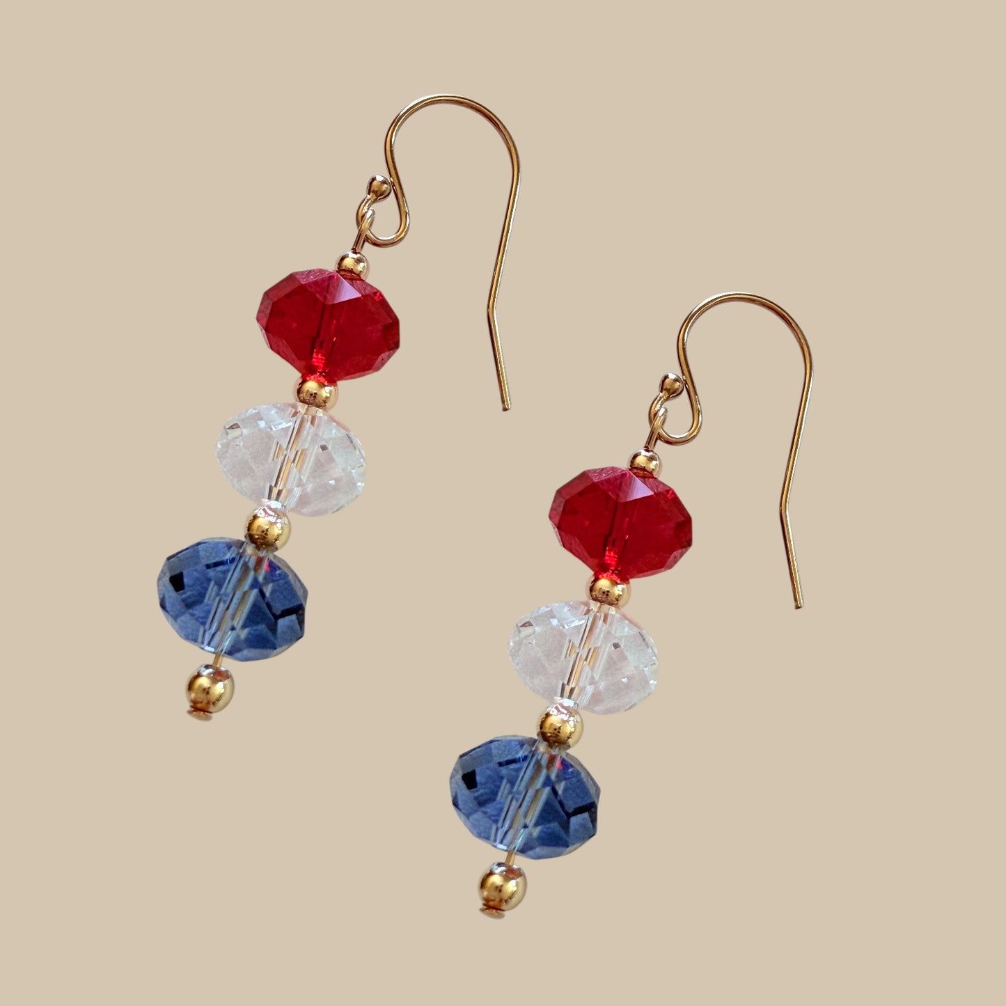 Pair of earrings with red, blue, and clear beads on a beige background