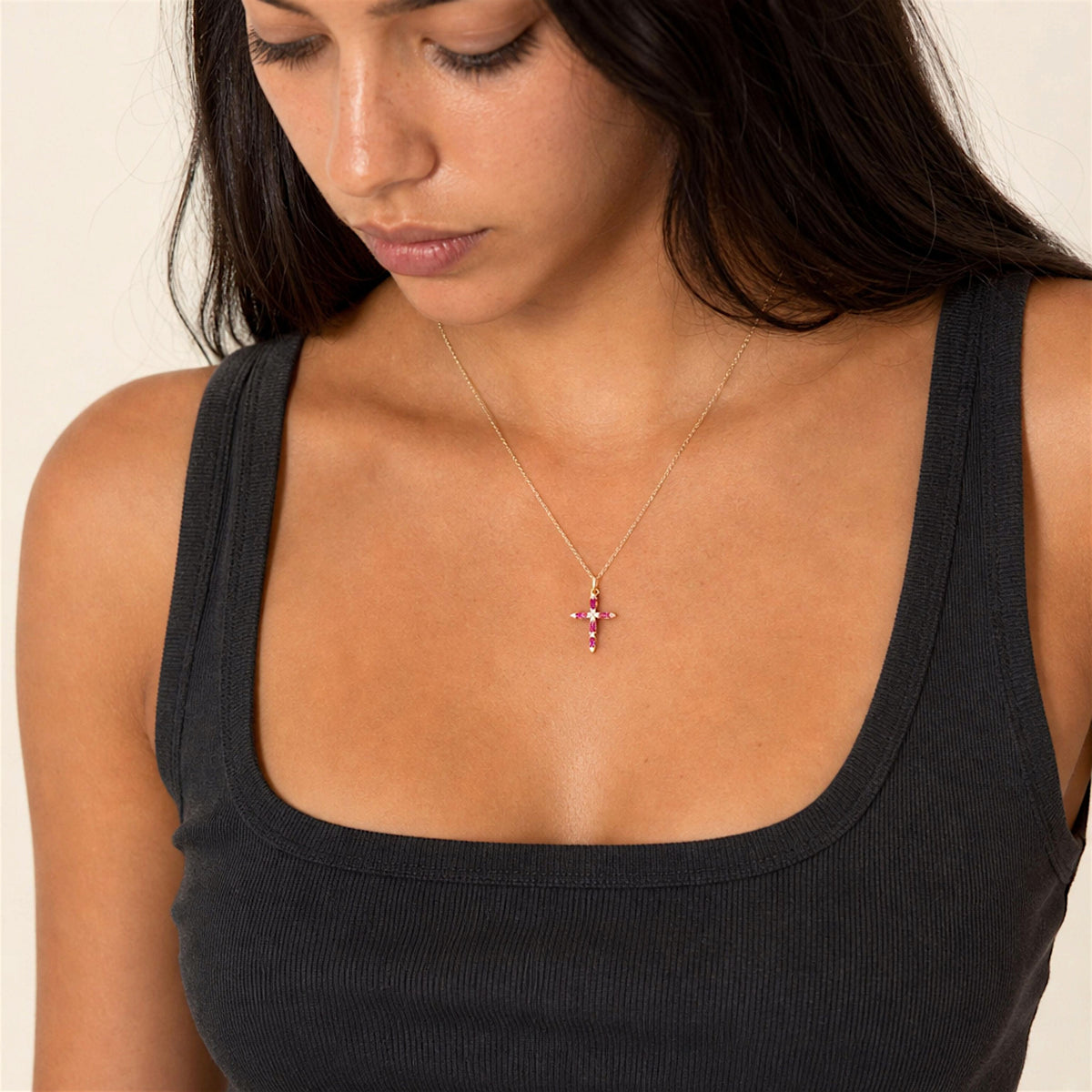 Model looking down while wearing a petite ruby and diamond cross necklace with a black top