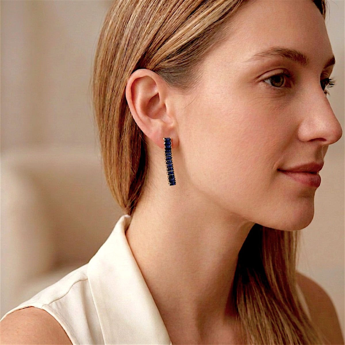 Woman wearing a sapphire-blue baguette CZ drop earring with gold-tone settings, shown in a side portrait.
