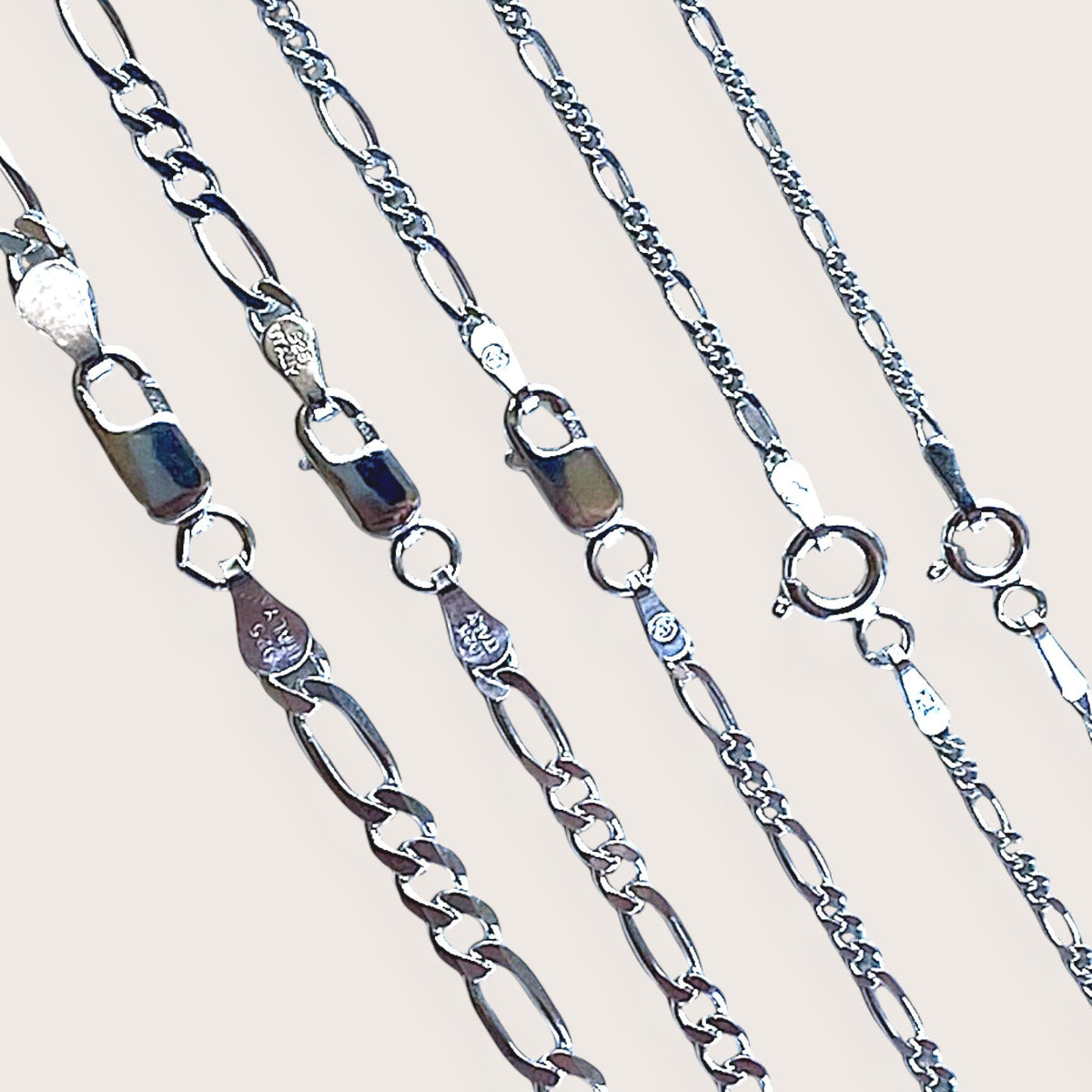 Close up of silver figaro chains with lobster and spring ring clasps - widths shown from 4mm to 1.5mm