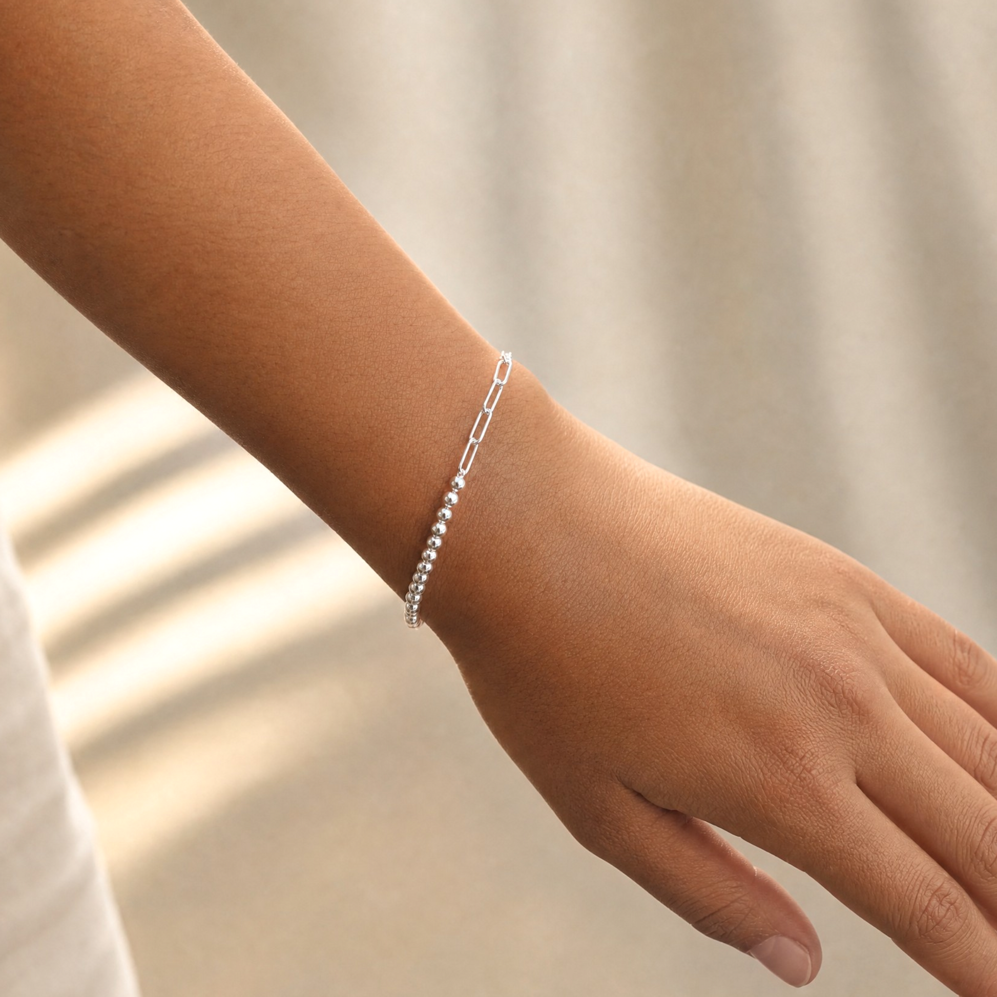 A delicate silver chain bracelet with small bead accents worn on a person's wrist, shown against a soft beige background.