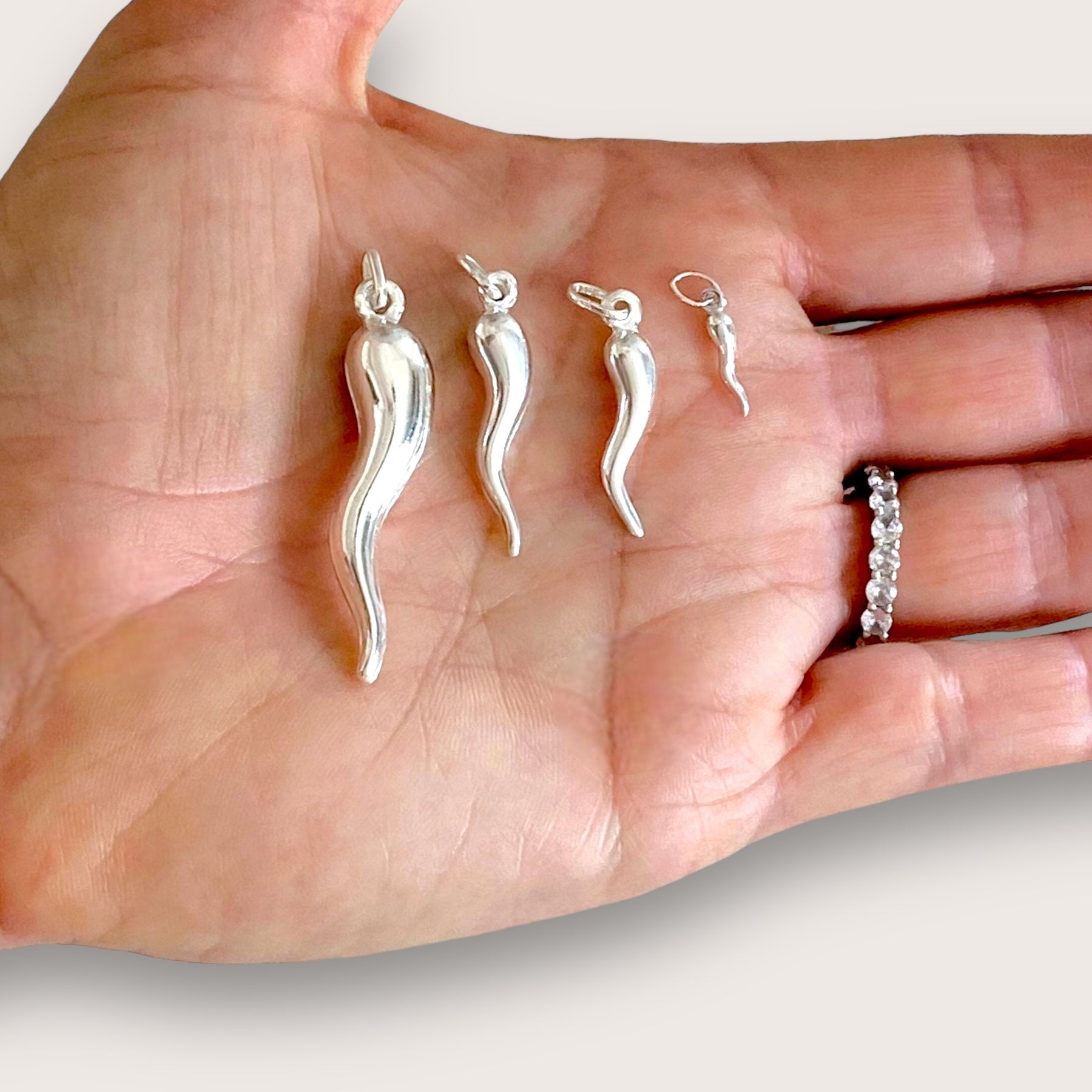 Hand model holding all four sizes of the high-polished 925 sterling silver Italian horn charms—often referred to as a lucky chili pepper pendant—in an open palm to display scale.