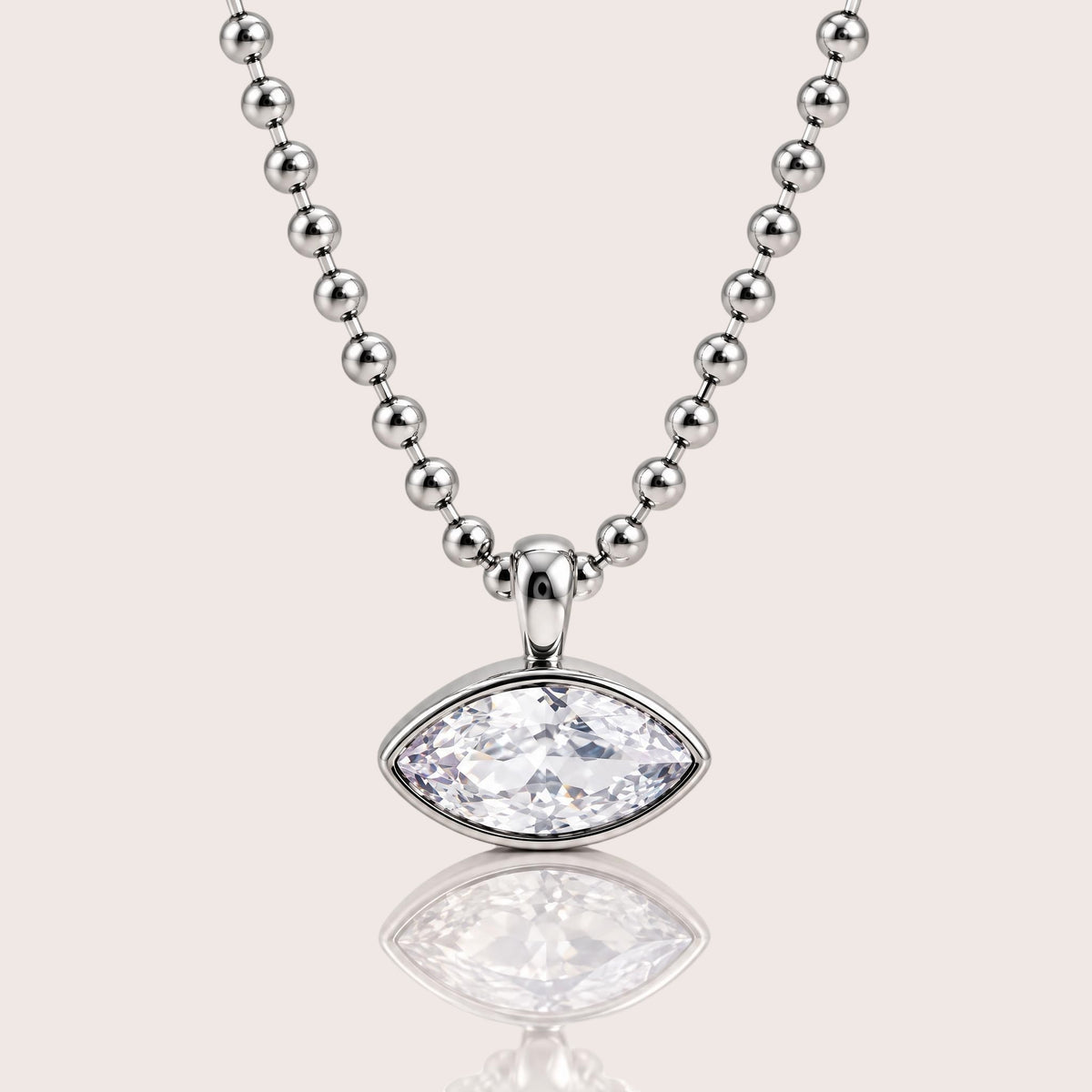 A silver beaded necklace with a marquise-cut clear gemstone pendant, displayed on a light beige background with a soft reflection below.
