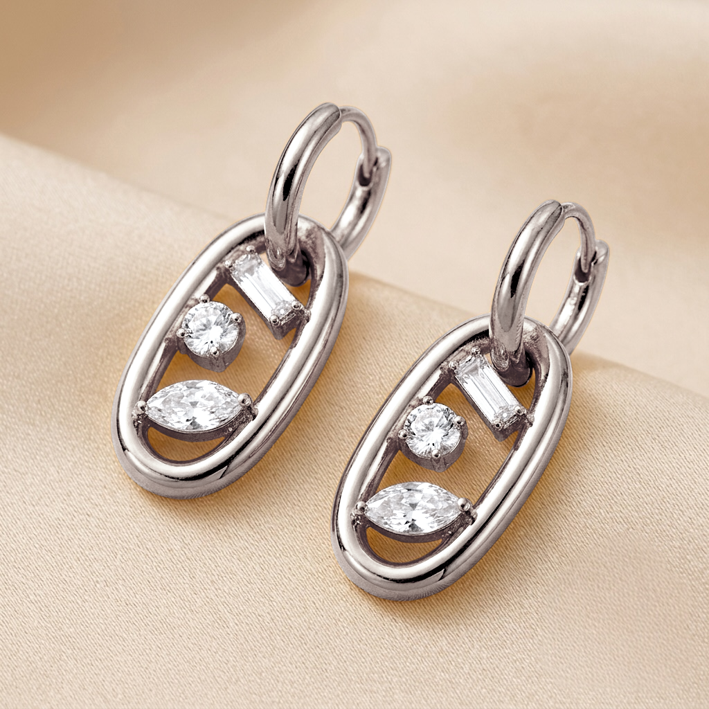 A pair of silver-toned drop earrings with marquise-cut and baguette-cut clear stones, displayed on a soft beige fabric background.