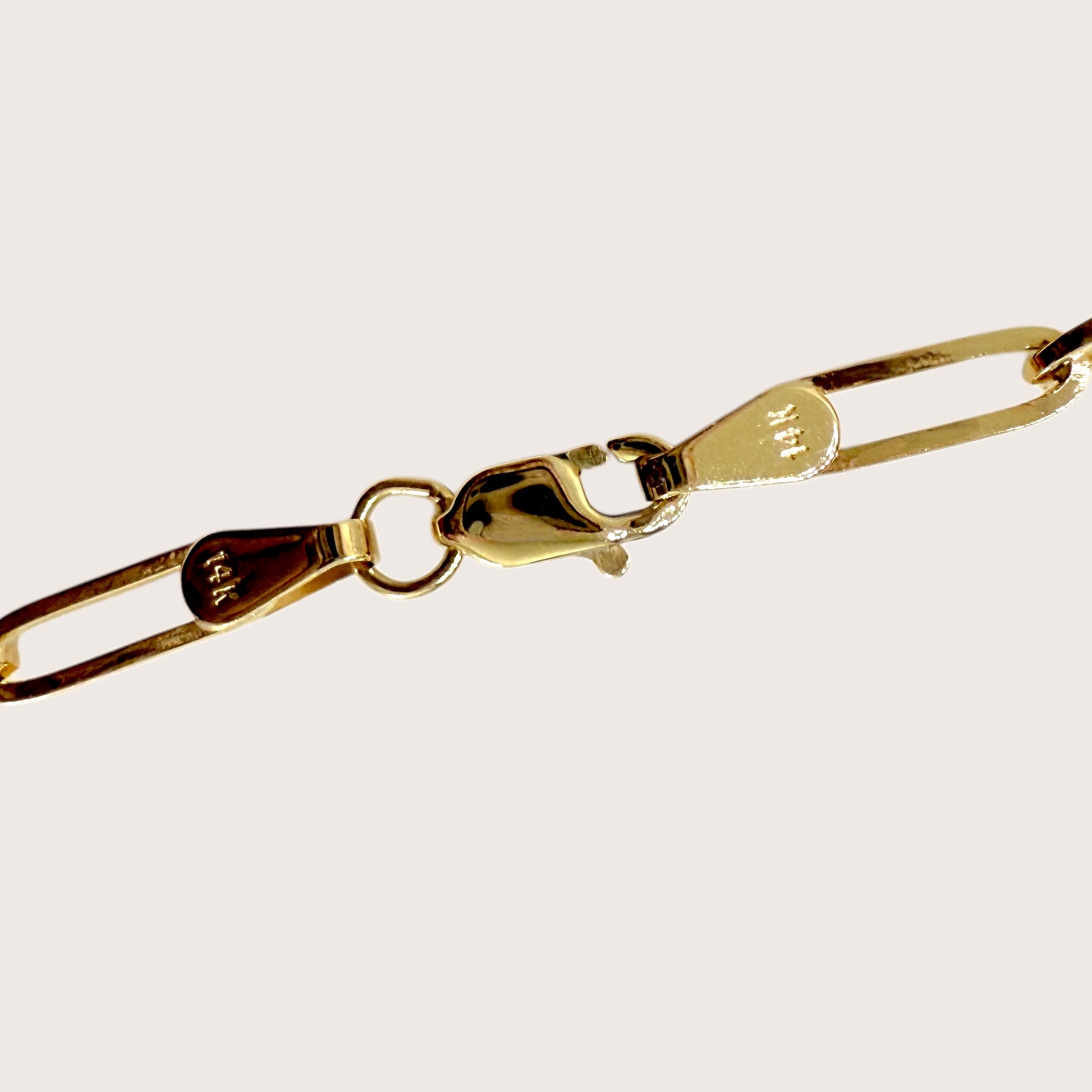 Close up of the paperclip bracelet in solid 14k gold, showing hallmark stamps of 14K and lobster clasp with soldered ends.