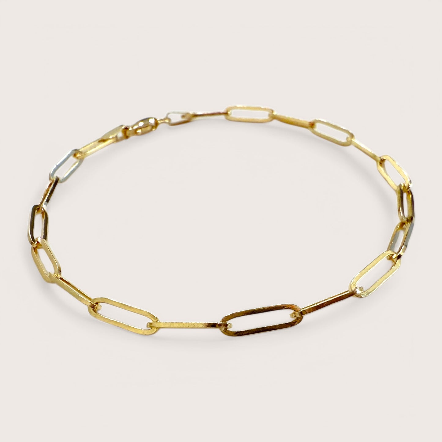 A close up of a 14K gold paperclip bracelet with interlinked elongated chain and a lobster clasp closure.