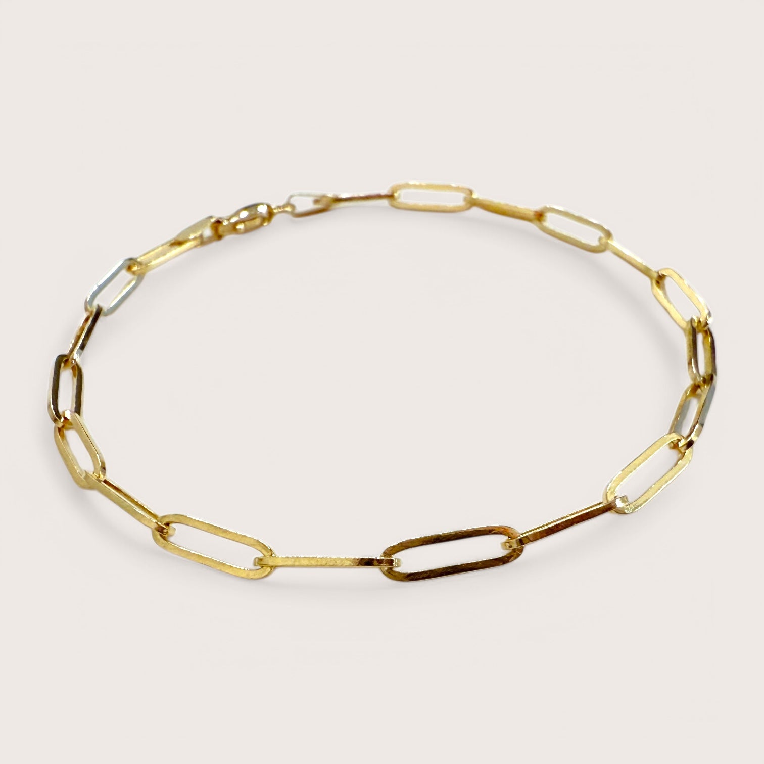 A close up of a 14K gold paperclip bracelet with interlinked elongated chain and a lobster clasp closure.